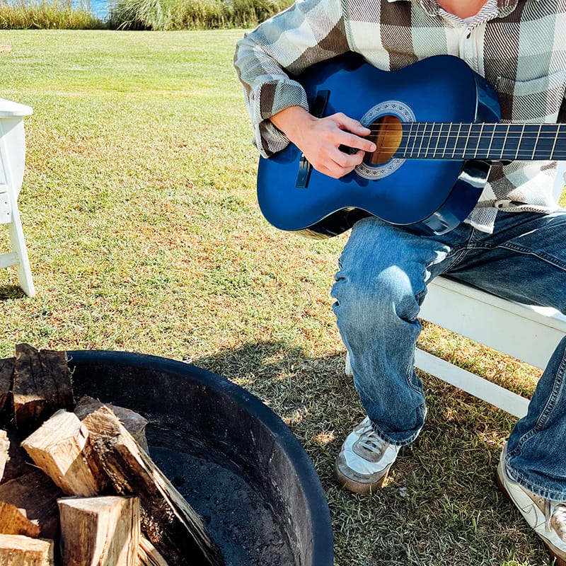 A person playing guitar by a fire pit at a Gulf Coast beach resort, creating a relaxed atmosphere