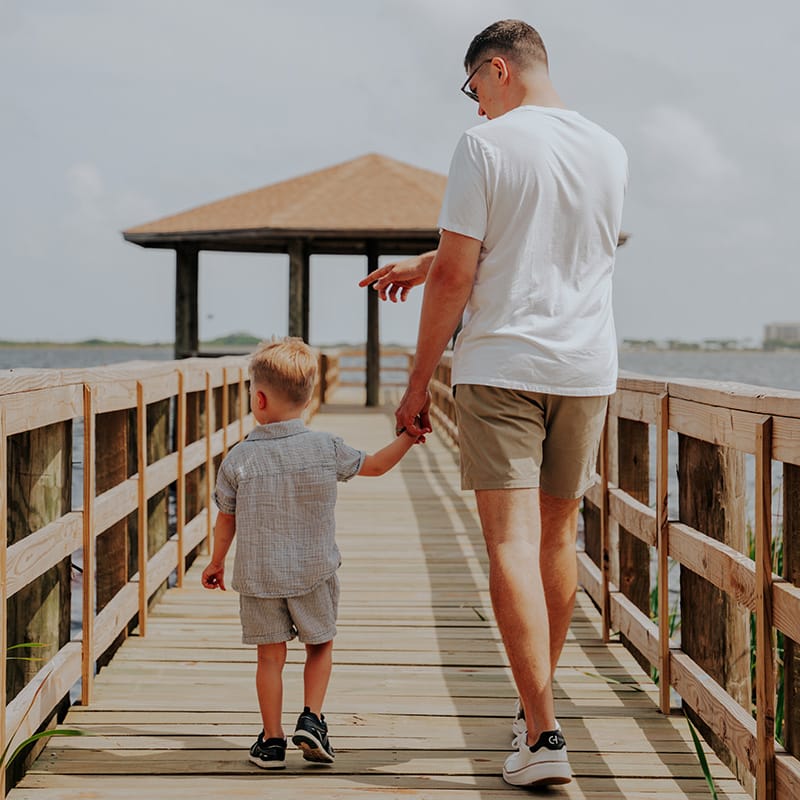 A father and son stroll along a boardwalk at a Gulf Coast beach resort, enjoying quality family time