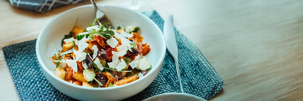 Close-up of a fresh salad topped with shaved parmesan, olives, and vegetables on a restaurant table.